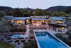 A residence emits warm light through its windows and doors. It is surrounded by views of desert foliage and a pool. A residence emits warm light through its windows and doors. It is surrounded by views of desert foliage and a pool.