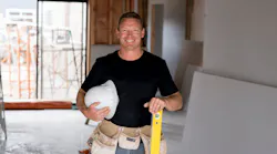 Smiling trade contractor holding hardhat and level on custom-home jobsite