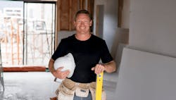 Smiling trade contractor holding hardhat and level on custom-home jobsite Smiling trade contractor holding hardhat and level on custom-home jobsite