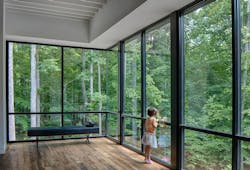 Girl looking into the woods from floor to ceiling windows Girl looking into the woods from floor to ceiling windows