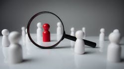 Black magnifying glass over red wooden figurine Black magnifying glass over red wooden figurine