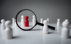 Black magnifying glass over red wooden figurine Black magnifying glass over red wooden figurine