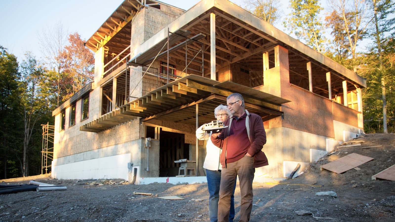 Homeowners stand in front of their custom home under construction holding an architect's model of the house