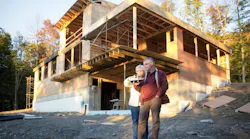 Homeowners stand in front of their custom home under construction holding an architect's model of the house