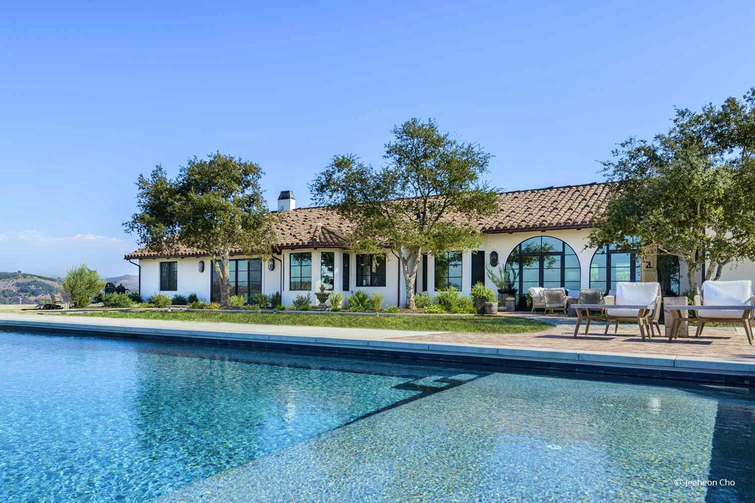 An Italian and Spanish-influenced home sits near a pool and features varied windows and doors across its fa&ccedil;ade.