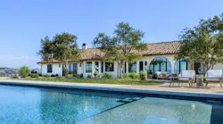 An Italian and Spanish-influenced home sits near a pool and features varied windows and doors across its façade.