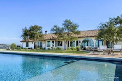 An Italian and Spanish-influenced home sits near a pool and features varied windows and doors across its façade. An Italian and Spanish-influenced home sits near a pool and features varied windows and doors across its façade.