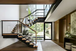 The stair rises through the double-height entry to a catwalk that crosses to the office, with the entry courtyard visible beyond.